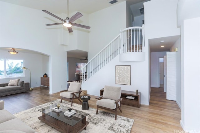 living area featuring stairway, arched walkways, wood finished floors, and a ceiling fan