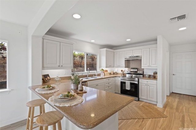 92-6012 Kohi St, Kapolei, HI 96707 - kitchen with stainless steel electric stove, under cabinet range hood, a breakfast bar, white cabinets, and recessed lighting