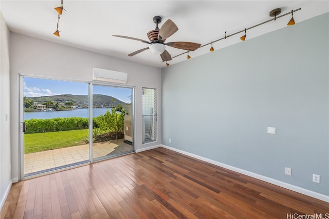 empty room with a wall mounted air conditioner, a water and mountain view, wood-type flooring, ceiling fan, and track lighting