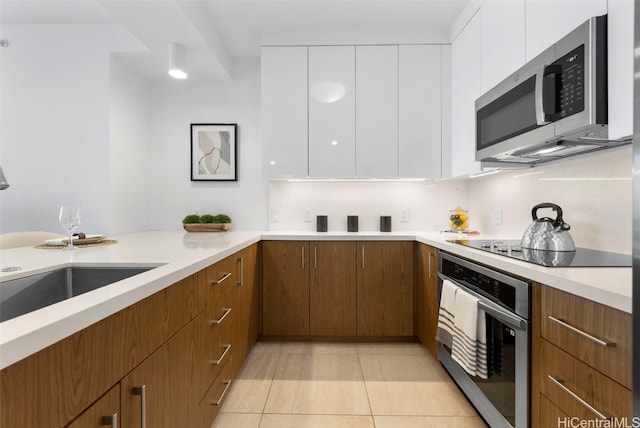 kitchen with sink, appliances with stainless steel finishes, white cabinetry, backsplash, and light tile patterned flooring