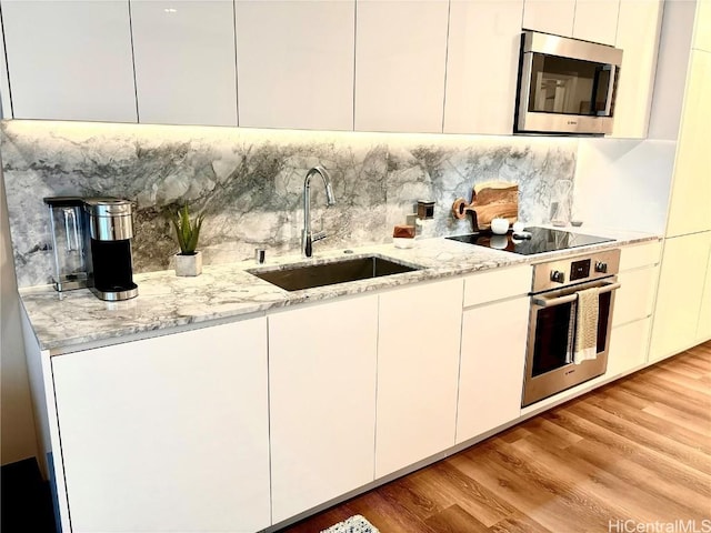 kitchen with sink, white cabinetry, light wood-type flooring, appliances with stainless steel finishes, and backsplash