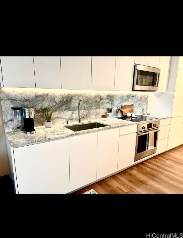 kitchen with light stone counters, sink, stainless steel appliances, and white cabinets