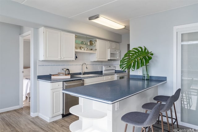 kitchen featuring sink, white appliances, kitchen peninsula, and white cabinets