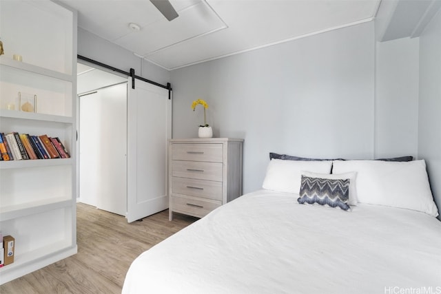 bedroom featuring a barn door, ceiling fan, and light wood-type flooring