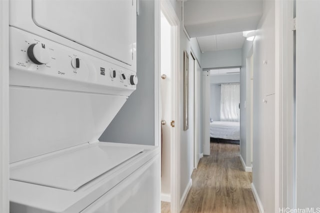 laundry room featuring stacked washing maching and dryer and light hardwood / wood-style flooring