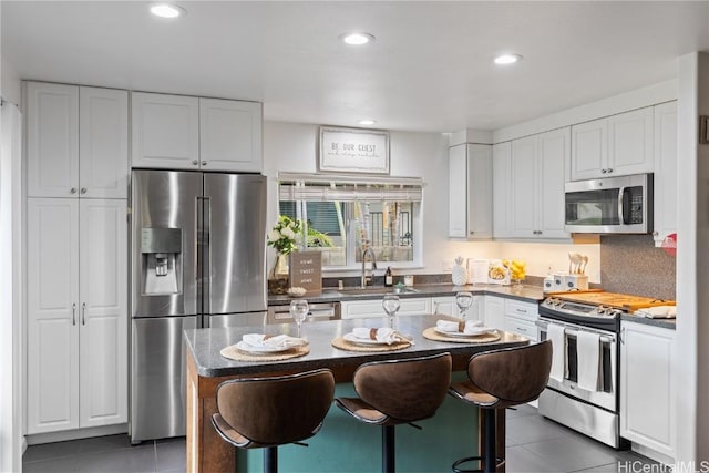 kitchen with a kitchen island, appliances with stainless steel finishes, white cabinetry, dark tile patterned flooring, and a kitchen bar