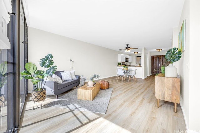 living area with light wood finished floors, baseboards, and a ceiling fan