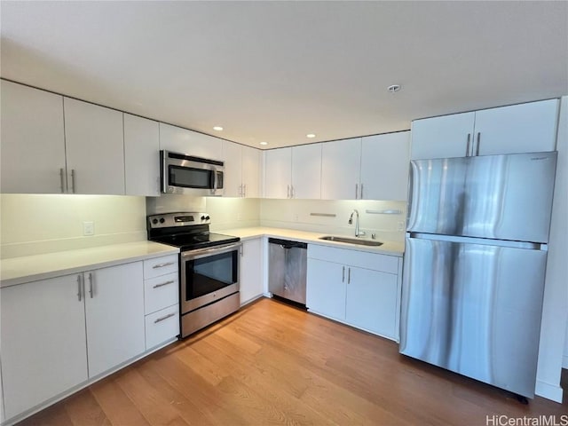 kitchen featuring appliances with stainless steel finishes, sink, white cabinets, and light wood-type flooring