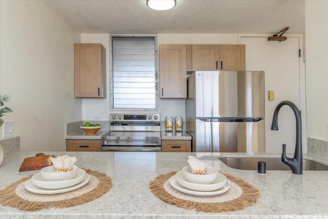 kitchen with appliances with stainless steel finishes, sink, light brown cabinetry, and a textured ceiling