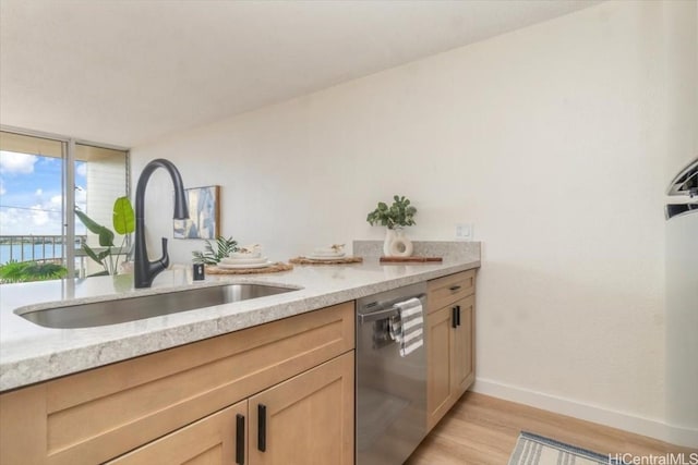 kitchen featuring light brown cabinetry, sink, light stone counters, light wood-type flooring, and stainless steel dishwasher