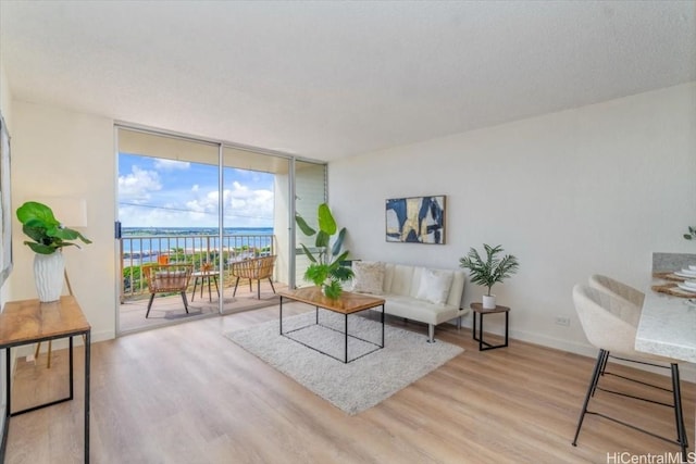 living room featuring light wood-type flooring, floor to ceiling windows, and a water view