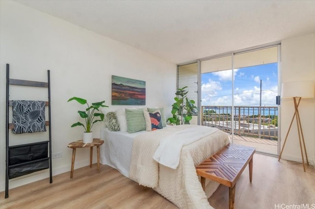 bedroom with light hardwood / wood-style flooring, access to outside, expansive windows, and a water view