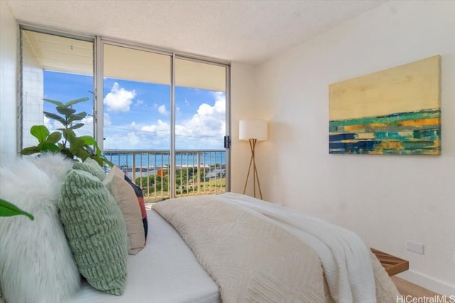 bedroom with access to exterior, a water view, a textured ceiling, and a wall of windows