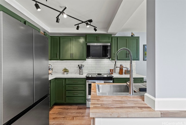 kitchen with appliances with stainless steel finishes, sink, green cabinets, and wood-type flooring