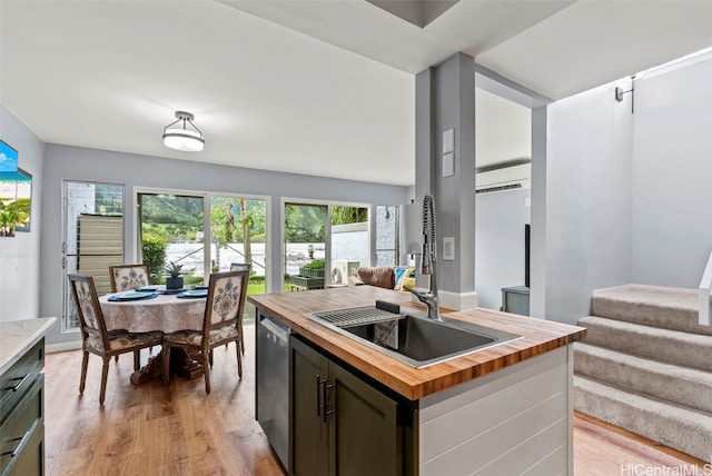 kitchen with butcher block counters, dishwasher, light wood-type flooring, sink, and a kitchen island with sink