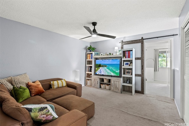 carpeted living room with a textured ceiling, a barn door, and ceiling fan