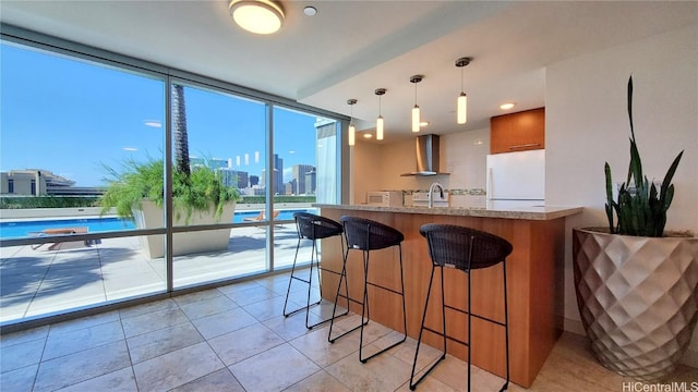 kitchen featuring decorative light fixtures, sink, a kitchen bar, white refrigerator, and wall chimney range hood