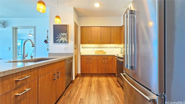 kitchen featuring appliances with stainless steel finishes, decorative light fixtures, sink, light stone countertops, and light hardwood / wood-style flooring