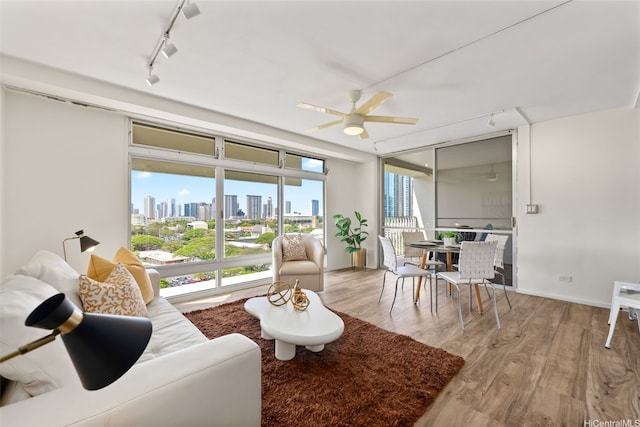 living area with track lighting, a view of skyline, light wood-type flooring, and a ceiling fan