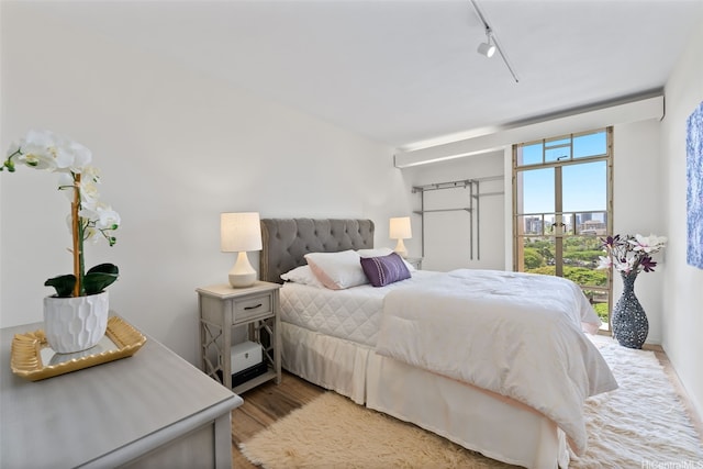 bedroom featuring track lighting, wood finished floors, baseboards, and access to outside