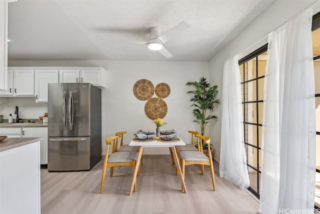 dining area with ceiling fan, sink, light hardwood / wood-style flooring, and a textured ceiling