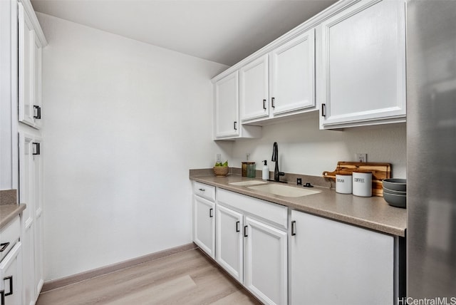 kitchen featuring white cabinetry, sink, stainless steel fridge, and light wood-type flooring