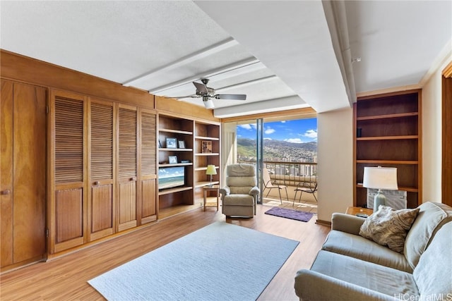 living room featuring beam ceiling, built in features, ceiling fan, and light hardwood / wood-style flooring