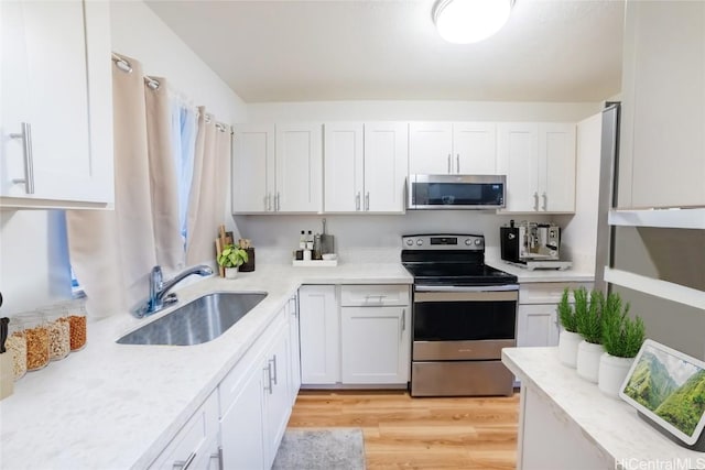 kitchen featuring sink, white cabinetry, light stone counters, light hardwood / wood-style flooring, and appliances with stainless steel finishes