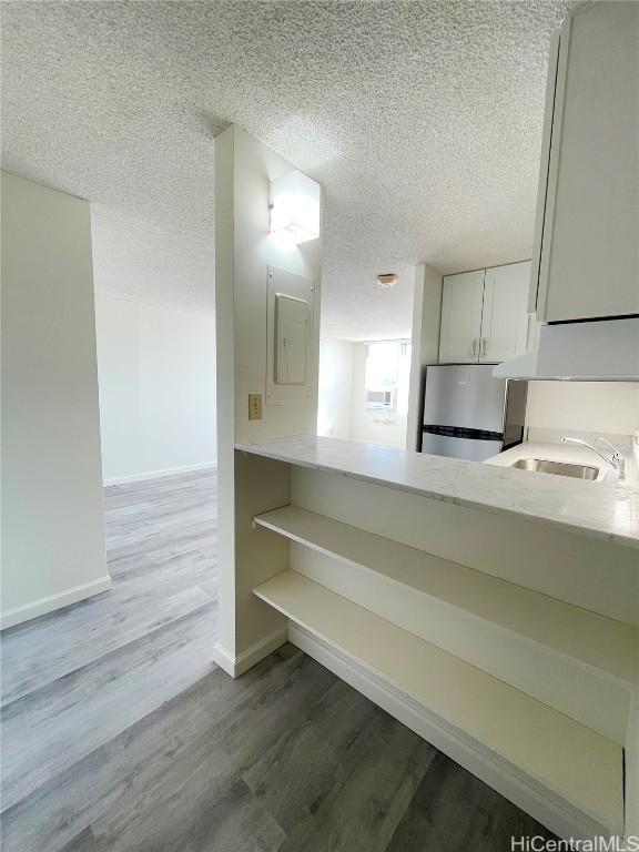 kitchen with sink, stainless steel fridge, white cabinetry, hardwood / wood-style floors, and a textured ceiling