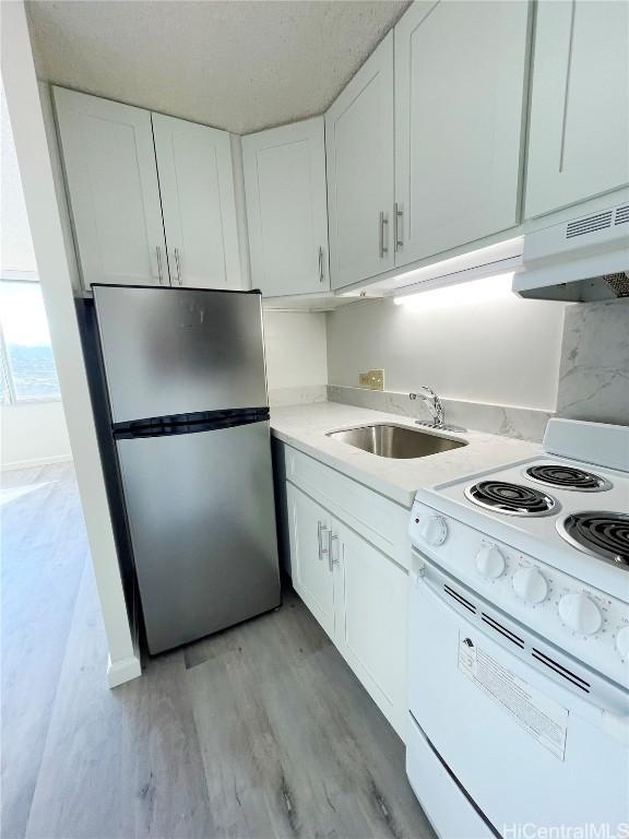 kitchen with stainless steel refrigerator, sink, white cabinets, white electric range oven, and light wood-type flooring