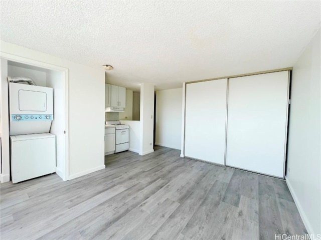 unfurnished living room with stacked washer and dryer, light hardwood / wood-style floors, and a textured ceiling