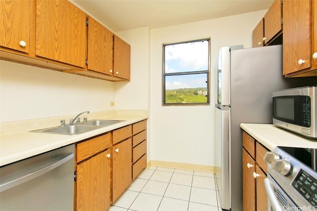 kitchen with light tile patterned flooring, a sink, light countertops, appliances with stainless steel finishes, and brown cabinets