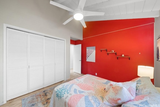 bedroom featuring ceiling fan, lofted ceiling with beams, a closet, and light wood-type flooring