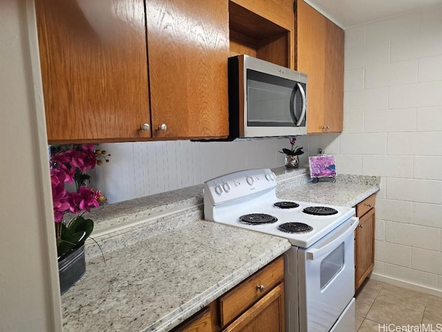 kitchen featuring light tile patterned floors, electric range, stainless steel microwave, and brown cabinetry