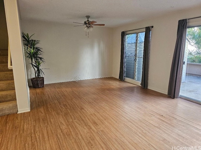 empty room with ceiling fan, stairway, baseboards, and wood finished floors