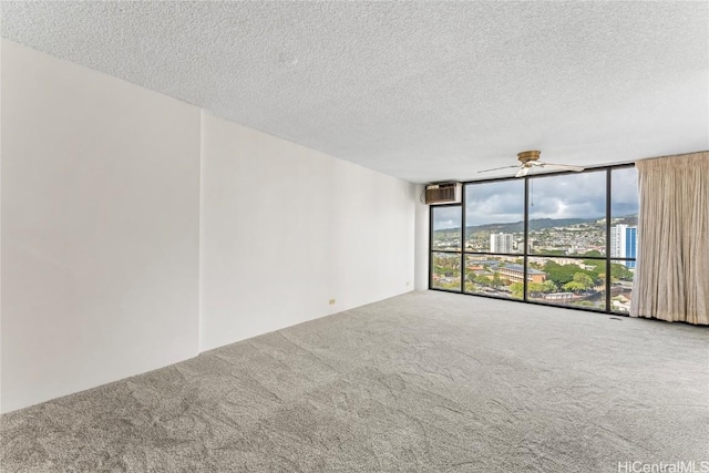 carpeted spare room with an AC wall unit, a textured ceiling, floor to ceiling windows, and ceiling fan