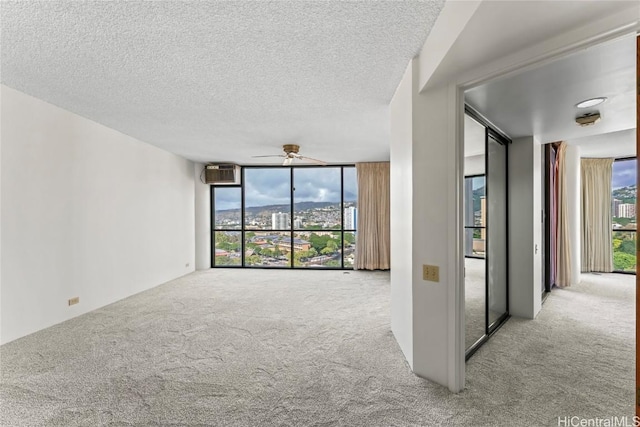 carpeted spare room with expansive windows, ceiling fan, a wall unit AC, and a textured ceiling