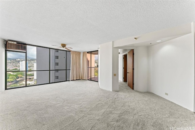 empty room featuring expansive windows, light colored carpet, ceiling fan, and a textured ceiling