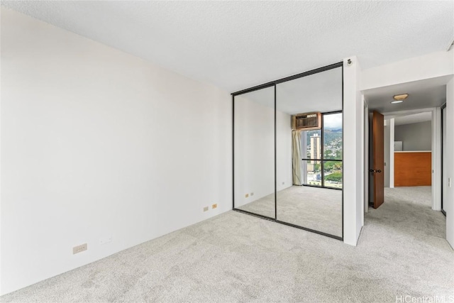 unfurnished bedroom featuring floor to ceiling windows, light colored carpet, a textured ceiling, and a closet