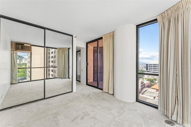 unfurnished bedroom with access to exterior, a wall of windows, light colored carpet, and a textured ceiling