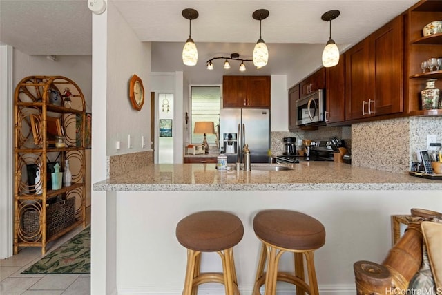 kitchen with stainless steel appliances, light stone counters, kitchen peninsula, and backsplash