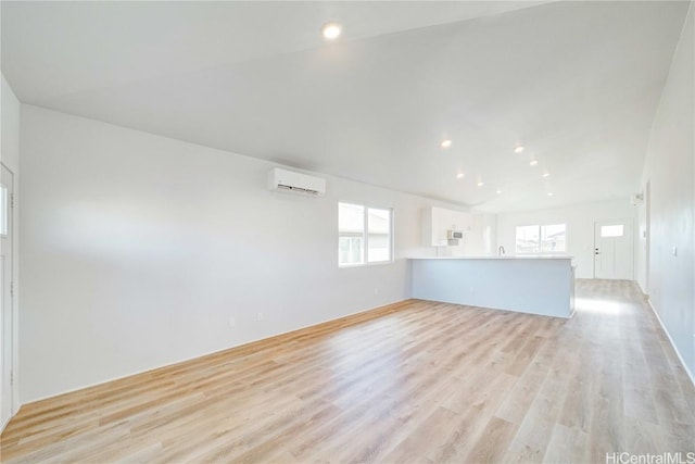 unfurnished room featuring sink, a healthy amount of sunlight, a wall mounted AC, and light wood-type flooring