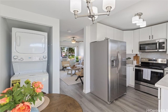 kitchen featuring stacked washer and dryer, stainless steel appliances, white cabinets, and light wood-type flooring