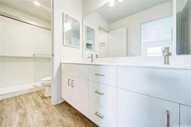 full bathroom featuring double vanity, toilet, a shower stall, a sink, and wood finished floors