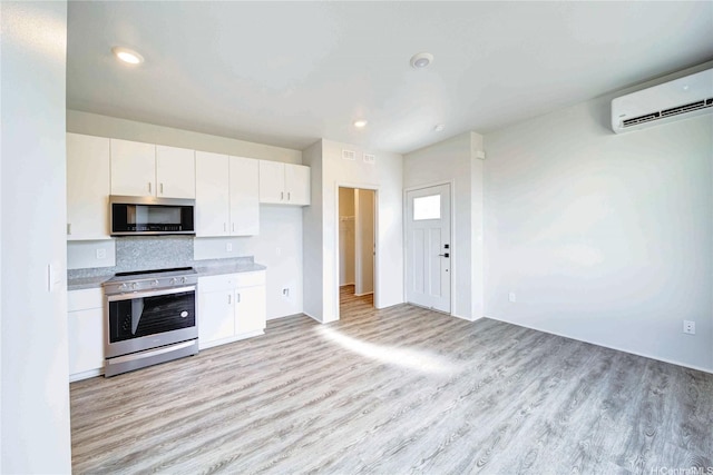 kitchen with light wood-type flooring, light countertops, white cabinets, a wall unit AC, and appliances with stainless steel finishes