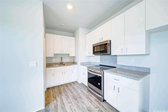kitchen featuring light countertops, white cabinets, light wood-style floors, stainless steel appliances, and a sink