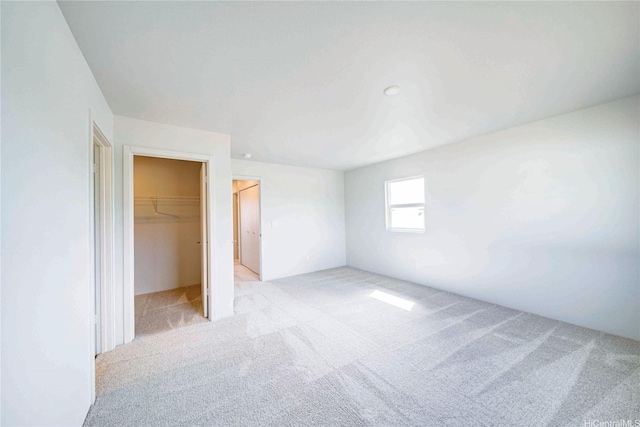 unfurnished bedroom with a closet, light colored carpet, and a walk in closet