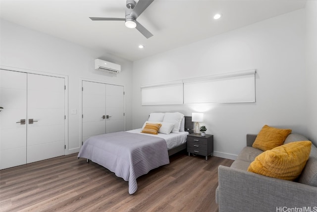 bedroom featuring multiple closets, dark hardwood / wood-style floors, a wall mounted air conditioner, and ceiling fan