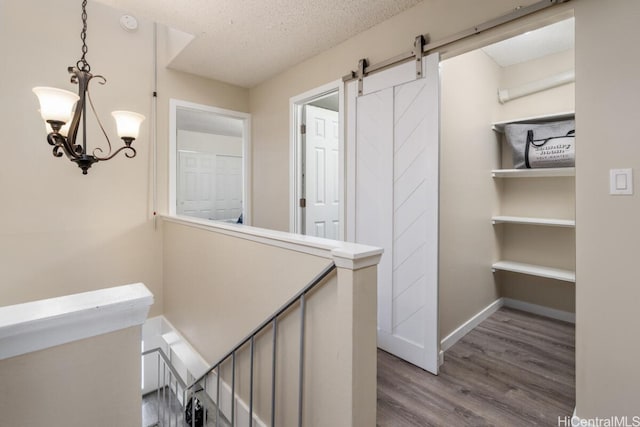 hall with a textured ceiling, a barn door, wood finished floors, an upstairs landing, and baseboards