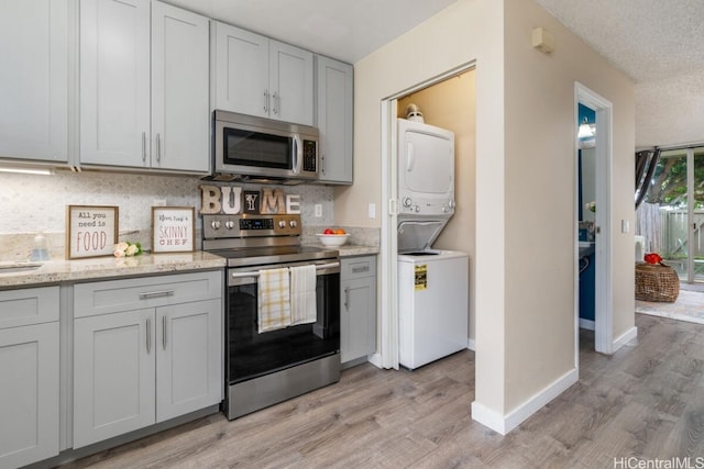 kitchen featuring stacked washer and dryer, baseboards, light wood-style floors, appliances with stainless steel finishes, and decorative backsplash